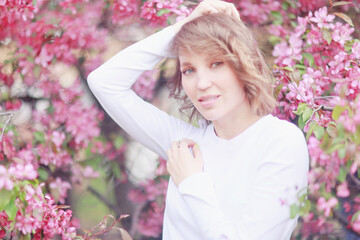 Fototapeta premium Springtime background, a woman in pink in a blooming cherry orchard, a model posing in a romantic style