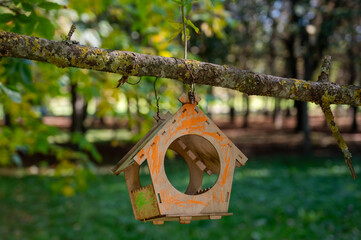 Painted wooden birdhouse hanging on tree branch among green leaves in summer garden