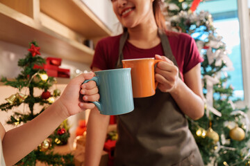 Holiday Toast. Mother and daughter clinking mugs in festive kitchen.