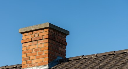 brick chimney on a tiled roof under clear blue sky in bright daylight