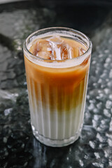 Iced coffee latte with layers of espresso, milk, and ice on a dark table, a refreshing and cool beverage
