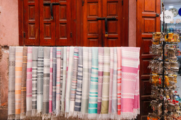 Colorful Moroccan bracelets and fabrics displayed for sale in front of a traditional wooden gate, reflecting vibrant street market culture.