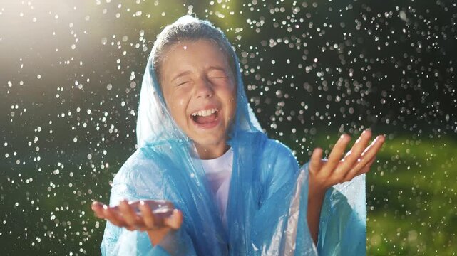 A child in a raincoat stands under raindrops. Happy family kid heavily dream. concept. Girl in a raincoat is raining and. smiling. The girl in the raincoat is smiling, it is raining.
