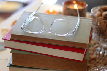 Lit candles, cookies, chocolate, nuts, tea, wine, pumpkins, books, reading glasses and autumn leaves on the table. Autumnal hygge at home. Selective focus.