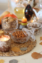 Lit candles, cookies, chocolate, nuts, tea, wine, pumpkins, books, reading glasses and autumn leaves on the table. Autumnal hygge at home. Selective focus.