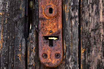 Old rusty keyhole in a vintage worn wooden door. Close up in old oxidized metal lock.