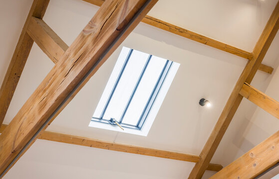 Skylight window in white sloped ceiling with oak beams, UK loft