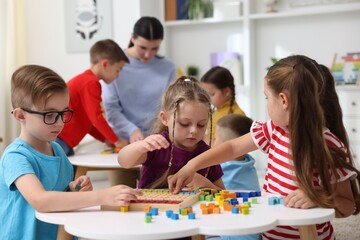 Cute children and teacher at white tables during lesson in elementary school