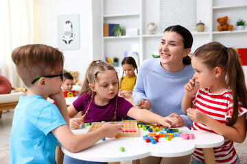 Fototapeta premium Cute children and smiling teacher at white table during lesson in elementary school