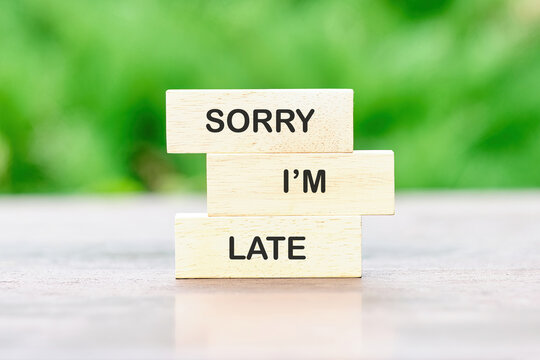 Stacked wooden blocks with a heartfelt message convey a genuine apology for being late. The scene features a natural green backdrop, emphasizing ease and sincerity
