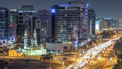 Fototapeta premium Mosque near Dubai Creek surrounded by modern buildings and busy traffic street day to night timelapse