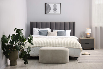 Large bed with linens, nightstand and houseplant near grey wall in bedroom. Interior design