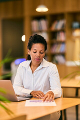 African American Woman Working at Desk With Laptop and Paper in Cozy Library Office