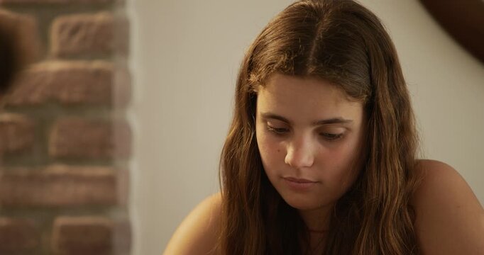Two siblings, a boy and a girl, teenagers playing cards at home. Girl facing forward, boy in foreshortening. Close-up of girl making faces.