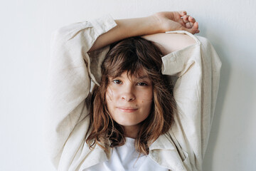 Fototapeta premium Adolescent girl in casual beige jacket posing relaxed against a white wall in a natural lifestyle portrait