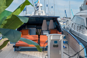 A vibrant and stylish yacht with bright orange sun loungers docked at the marina, connected to the shore power pedestal, blending modern design with comfort