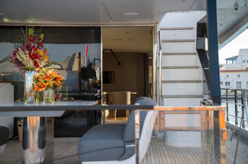 Elegant yacht interior with gray cushioned seating, modern table, glass railings, and fresh floral arrangements. Sunlight softly illuminates the cozy space, blending comfort with style.