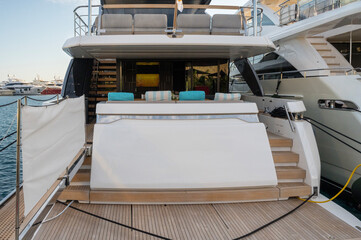 Luxury yacht stern deck with teak flooring, cushioned seating with turquoise and striped pillows. Modern stairs lead to upper deck at Limassol Marina.
