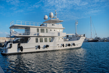 Large white yacht docked at marina. Multiple decks with railings and antennas on top. Other yachts visible in the background. Bright sunny day with reflections on the water  at Limassol Marina
