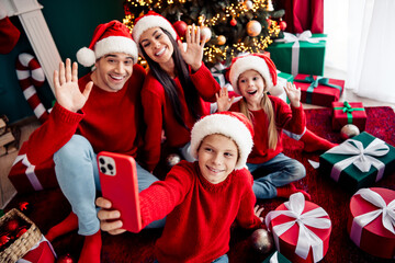 Joyful family celebrating Christmas together at home by the tree while taking a selfie and...