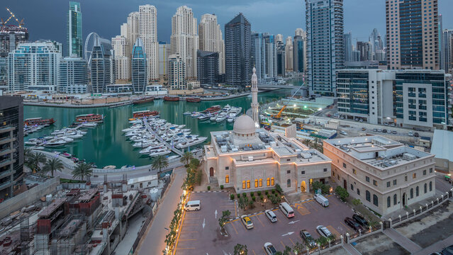 Yachts in Dubai Marina flanked by the Al Rahim Mosque and residential towers and skyscrapers aerial night to day timelapse.