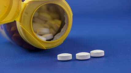 Bottle of white pills spilling onto a blue surface during a health-related scene