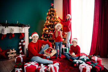 Festive family celebrating Christmas at home decorating tree and exchanging gifts surrounded by...