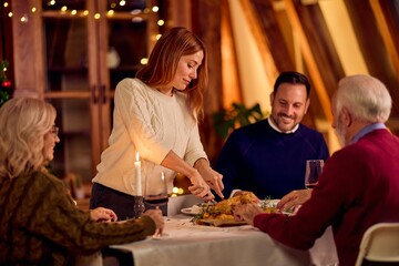 Warm Family Christmas Dinner: Woman Serving Food at Table with Friends and Laughter