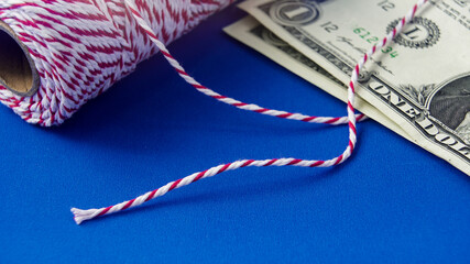 Red and white twine beside one dollar bill on blue background during a crafting session