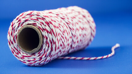 Red and white twine spool on a blue background, ideal for crafts and decoration projects