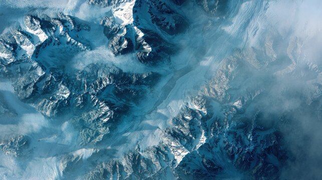 Aerial view of snow-covered mountain peaks partially obscured by clouds and a hazy atmosphere
