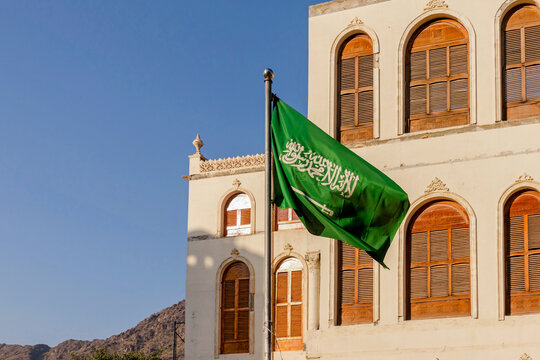 A Saudi Arabia flag in front of an ancient Arabic architectural building in a tourist attraction in the city of Taif, Saudi Arabia