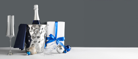 Ice bucket with bottle of champagne, glasses and Christmas gift on dark background