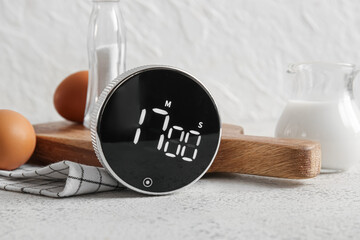 Modern kitchen timer and wooden tray with ingredients on light grunge table, closeup