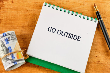 A notebook with a handwritten message invites everyone to go outside and enjoy the beauty of nature. Beside it, a roll of cash and a pen suggest spontaneity and adventure