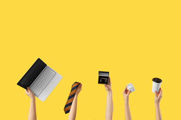 Young women holding modern laptop, cufflinks in box, earphones, paper cup and men's tie on yellow...