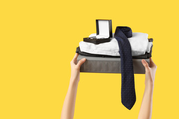 Young woman holding folder, cufflinks, men's tie, trousers and shirt on yellow background