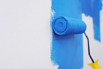 Roller Brush Painting, Worker painting on surface wall Painting apartment, renovating with blue color paint. Leave empty copy space white to write descriptive text beside.