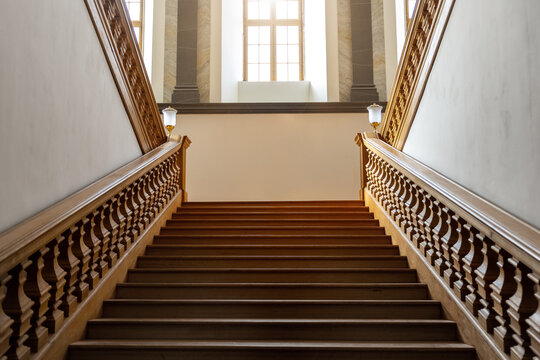 Elegant wooden vintage empty staircase rises toward large bright windows filled with warm light. Symmetrical balustrades and refined craftsmanship convey timeless elegance and architectural harmony