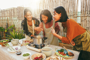 Asian family cooking thai food together at home patio outdoor - Mother and two daughters having fun preparing brot for dinner at house backyard - Main focus on mum face