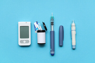 Digital glucometer, lancet pens and test strips in box on blue background