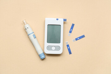Digital glucometer, test strips and lancet pen on beige background