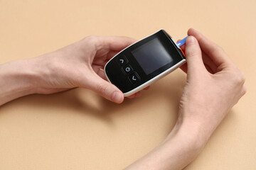 Young diabetic woman using digital glucometer on beige background