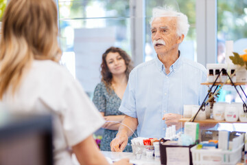 Fototapeta premium Senior man buying medicine from female pharmacist in pharmacy.