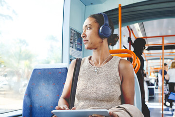Woman commuting on public transport listening to music and using tablet