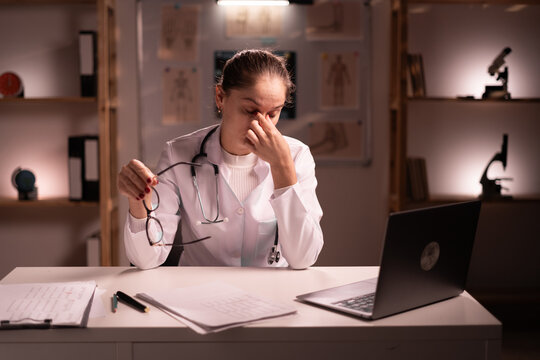 Tired woman doctor rubbing nose and eyes feeling fatigue and headache sitting at table and holding eyeglasses in clinic. stress and frustration concept.