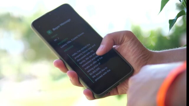 A persons hands on a balcony or terrace open and read a newly received message on a smartphone, scrolling through the text content carefully. This scene represents modern communication and information