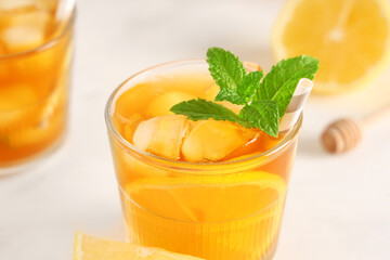 Glass of fruit tea with lemon and mint leaves on light background