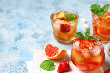 Glasses of cold tea with grapefruit, peach and strawberry slices on blue grunge background