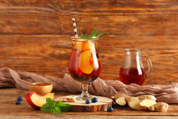 Glass of cold tea with peach slices, bilberries, mint leaves and ginger on wooden background